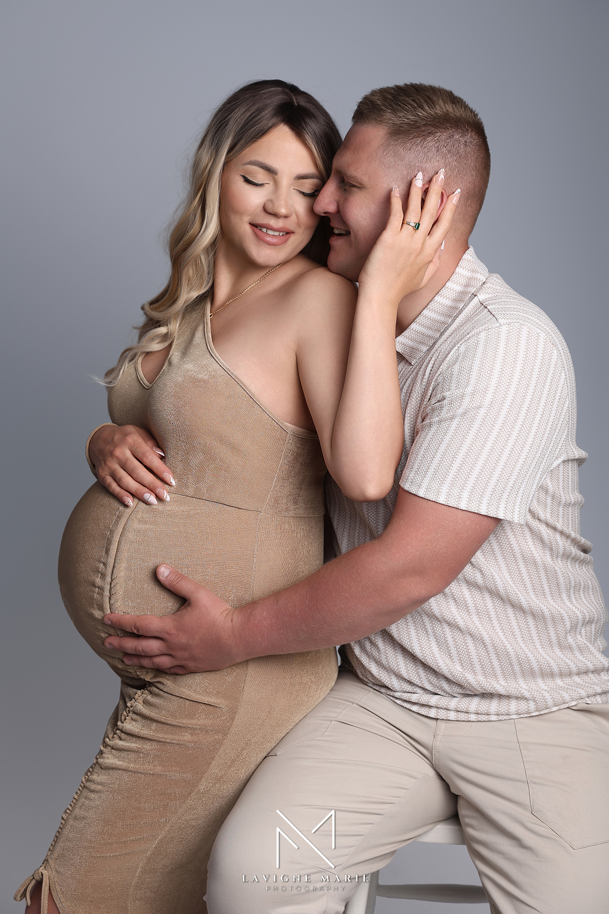 Elegant maternity couple posing in a studio photoshoot with soft lighting and timeless styling