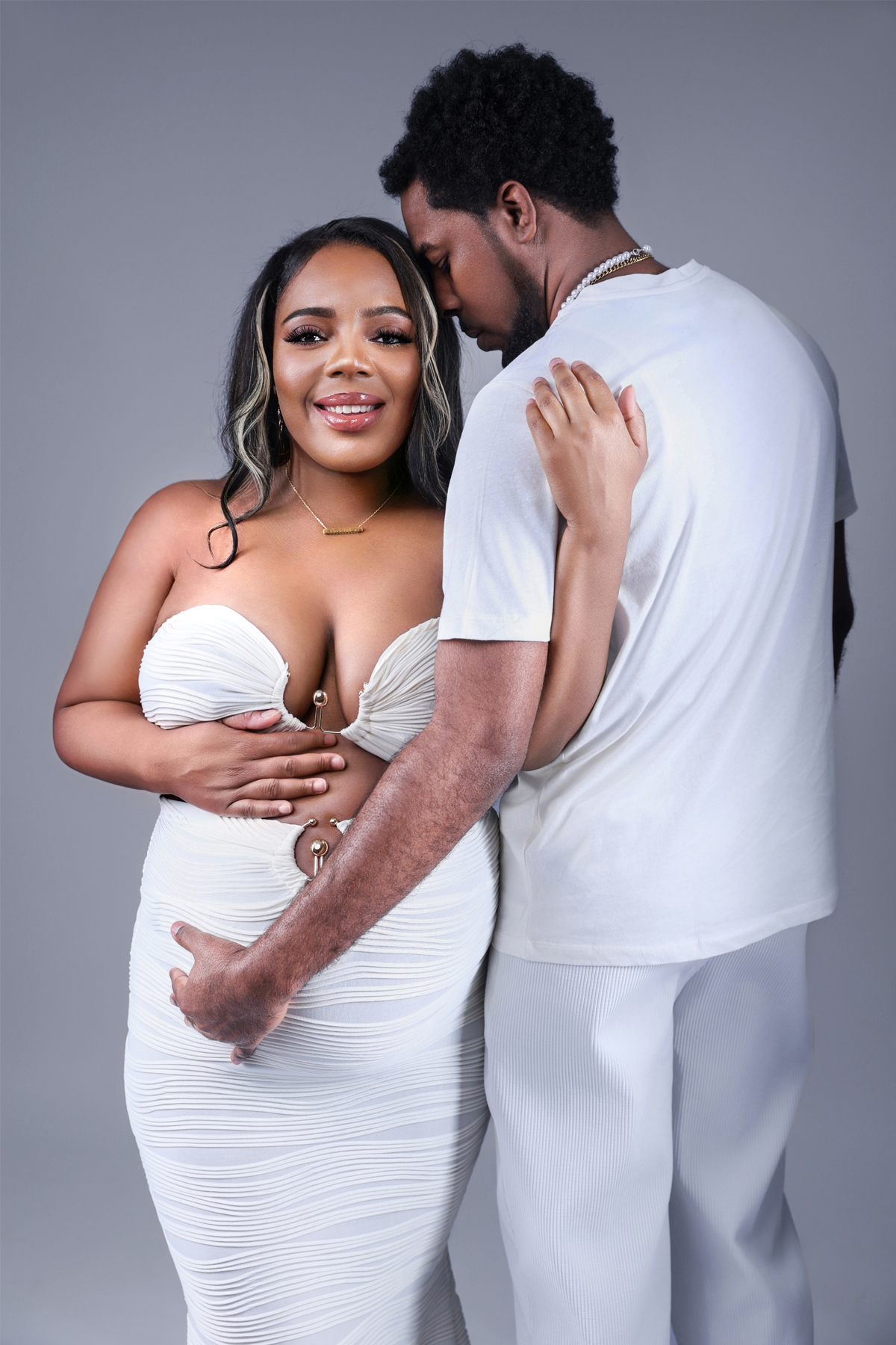 Maternity couple photoshoot in a studio showing expecting parents embracing and smiling while highlighting the baby bump.