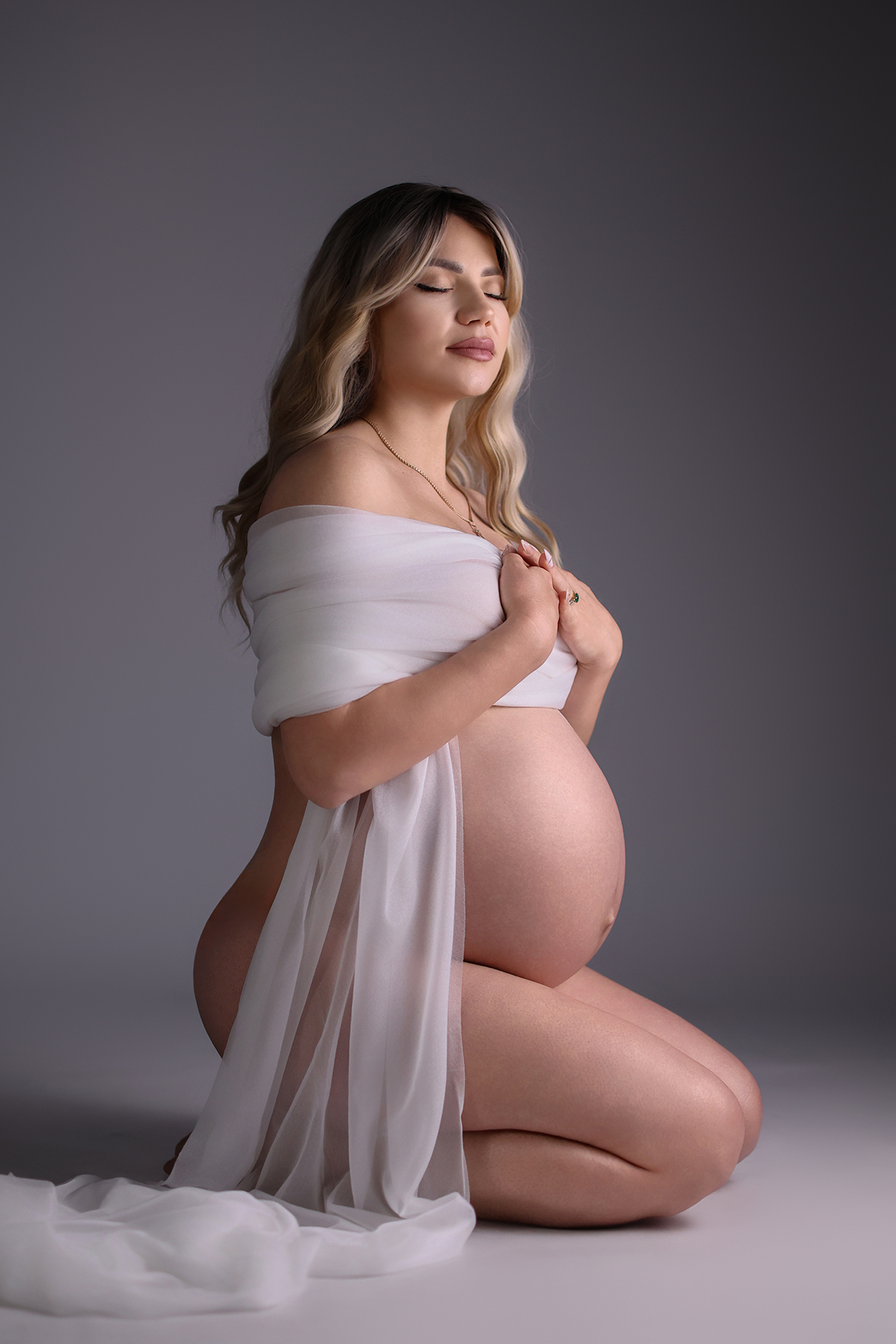 Maternity photography studio session with a pregnant woman posing gracefully against a neutral backdrop under professional studio lighting.