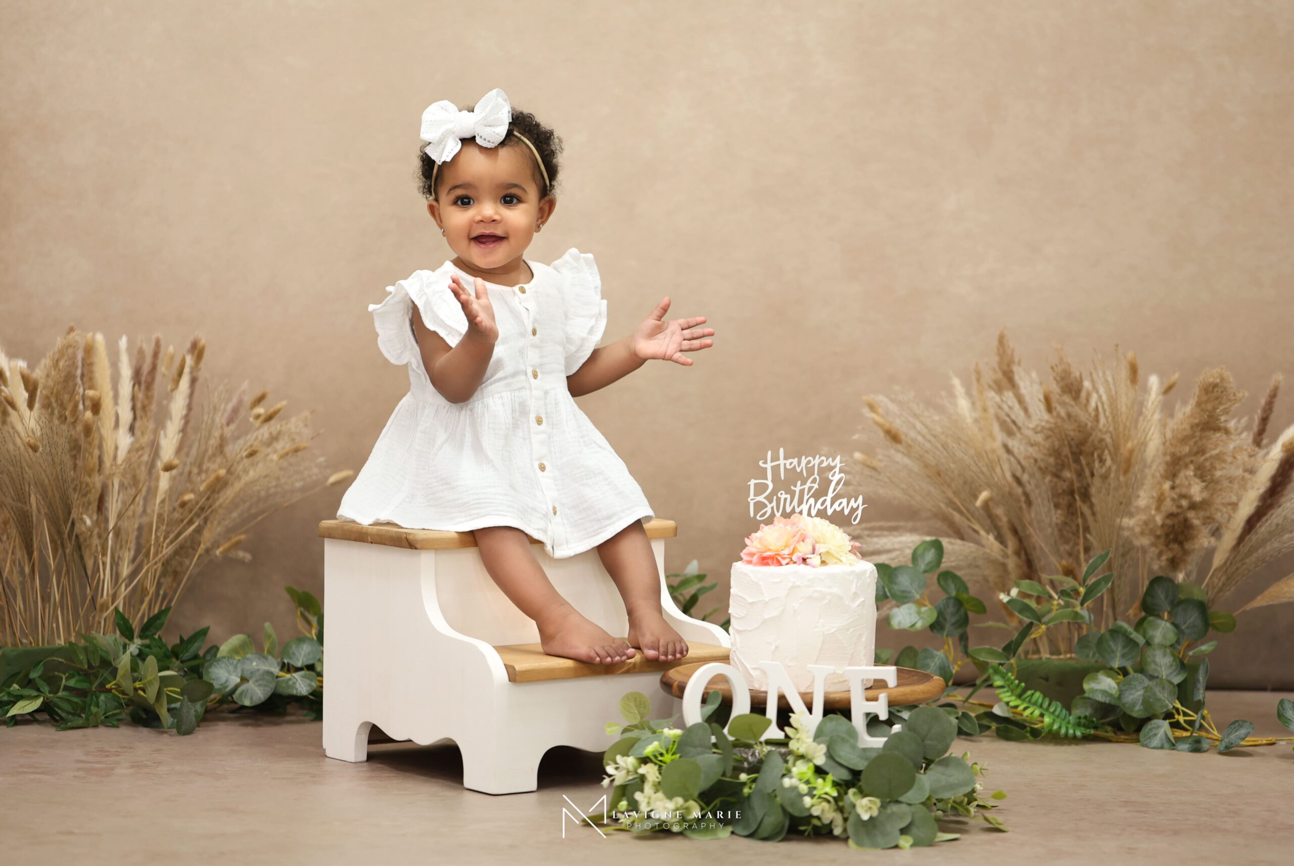Baby enjoying a smash the cake birthday photoshoot with frosting-covered hands and playful expression