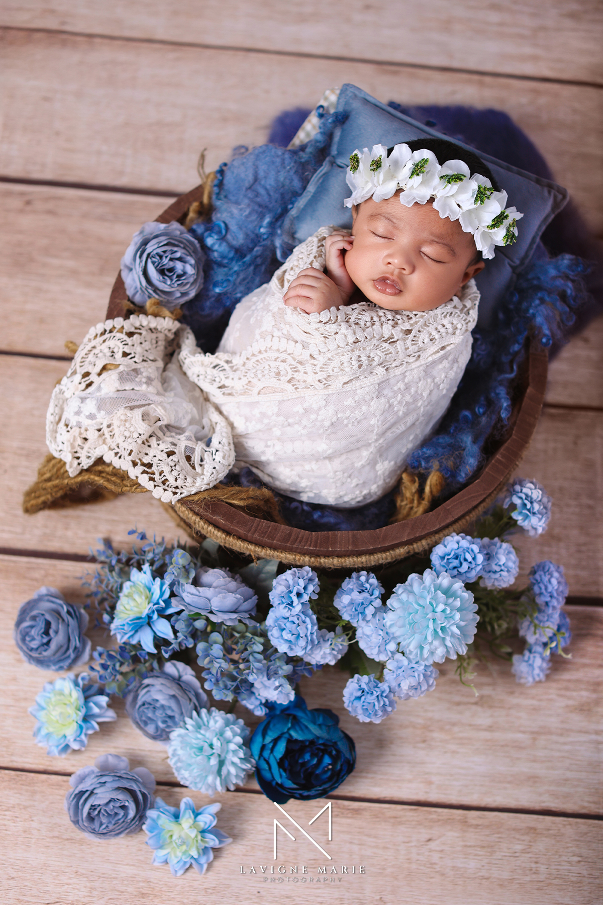 Newborn baby girl photoshoot wrapped in soft white lace blanket, delicate infant portrait with gentle lighting surrounded by flowers.