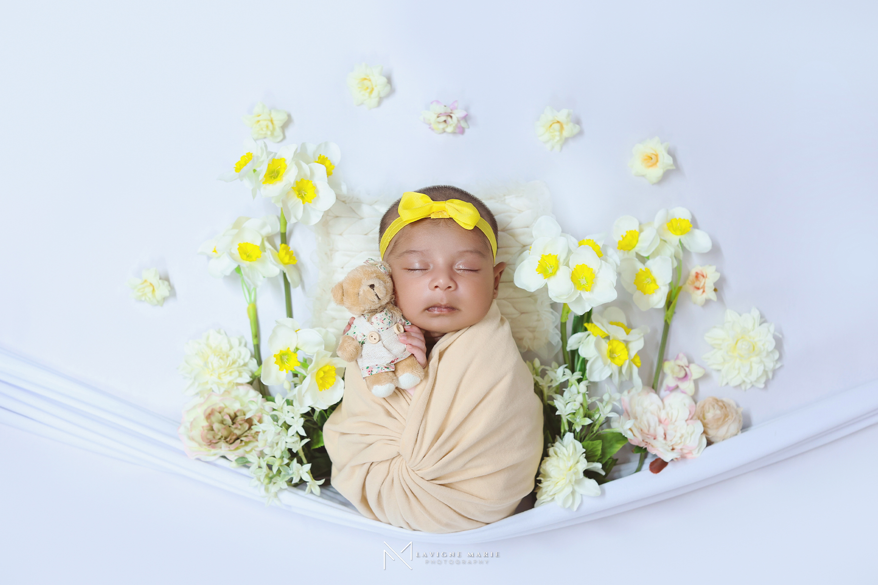 Spring theme newborn photoshoot by Lavigne Marie featuring a sleeping baby wrapped in cream fabric and surrounded by daffodils and soft floral accents.