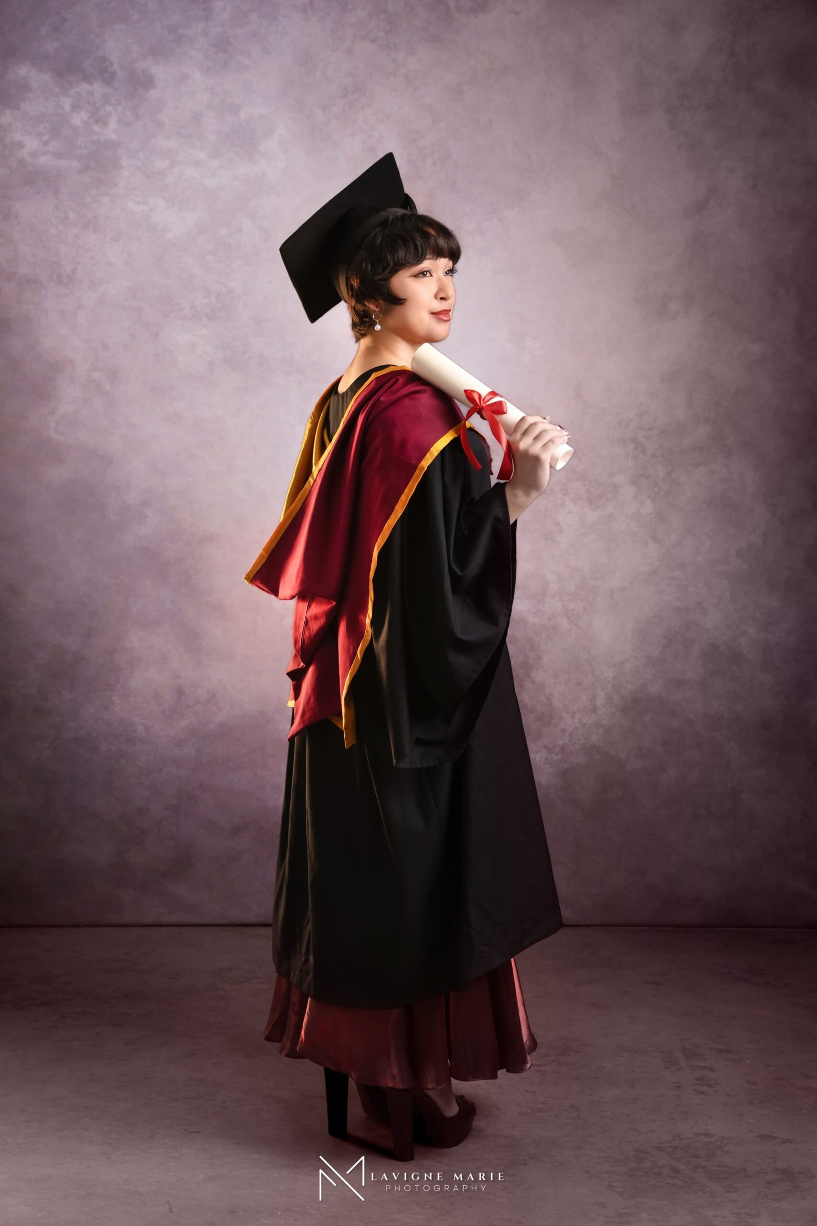 University graduation studio session in London with graduate wearing cap and gown posing for professional portraits in a photography studio